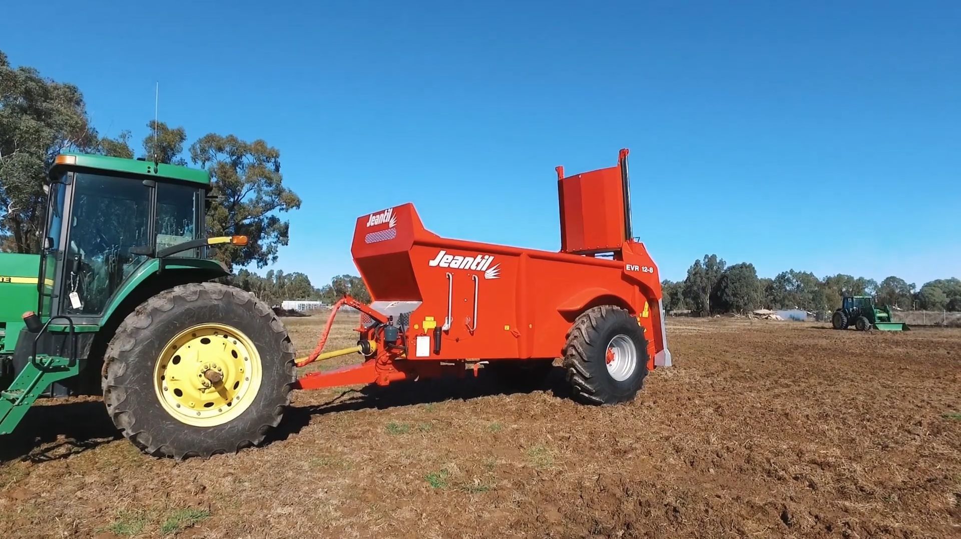 A green tractor is pulling a red trailer in a field.
