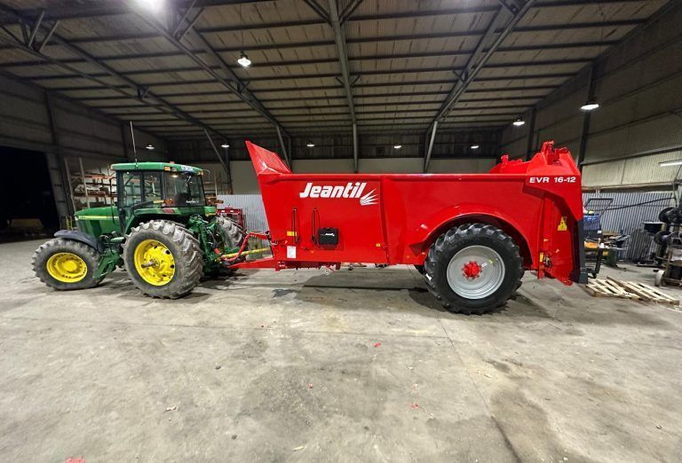 A john deere tractor is towing a red trailer in a warehouse.