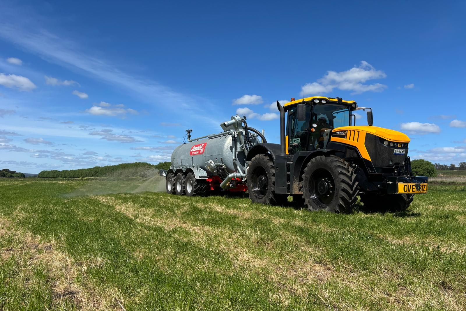 A john deere tractor is pulling a jentil slurry tanker in a grassy field.