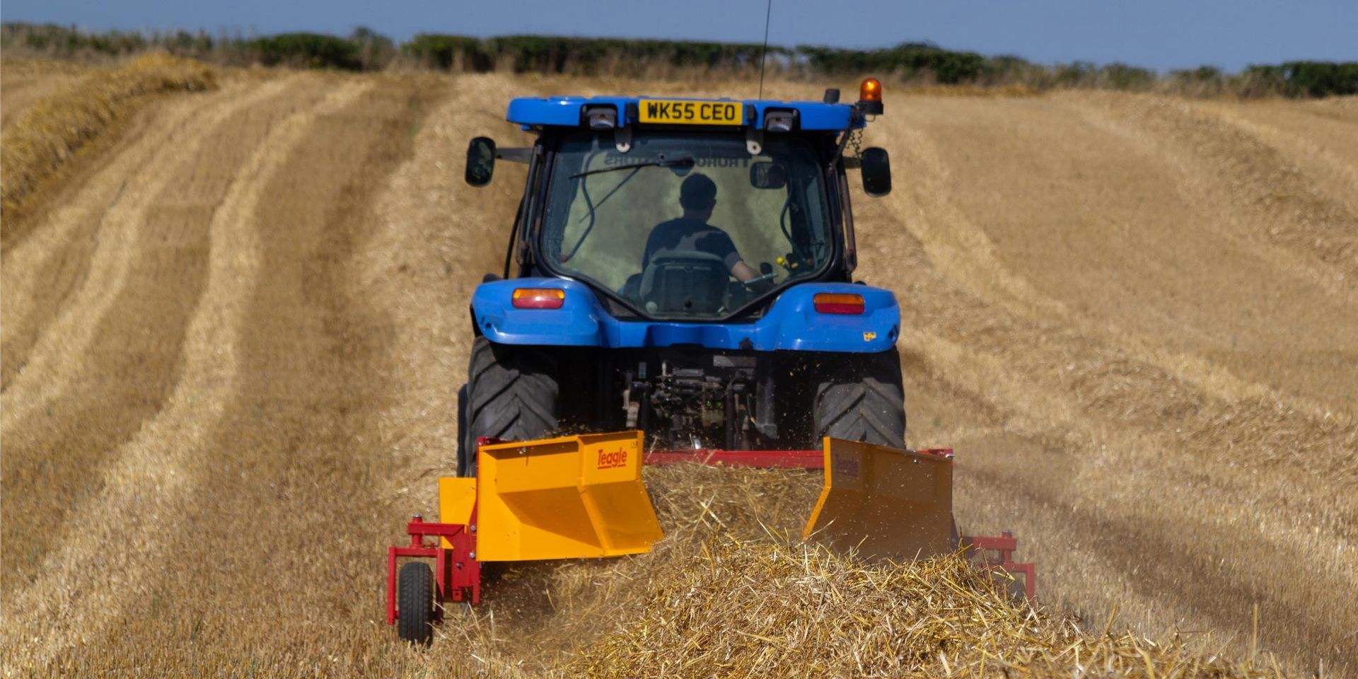A blue tractor is plowing a field of dry grass.