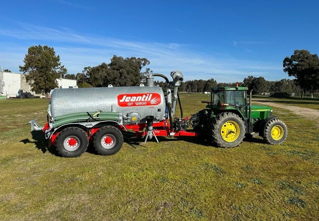 A john deere tractor is pulling a jentil slurry tanker in a grassy field.