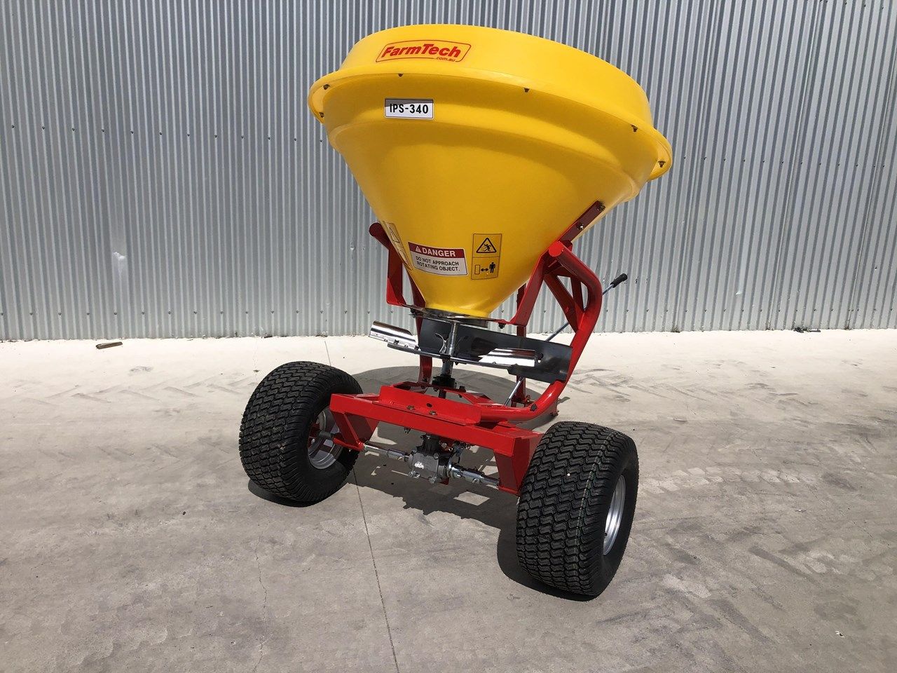 A yellow and red spreader is sitting on the ground in front of a metal wall.