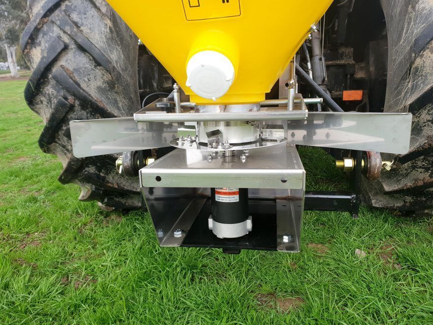 A yellow tractor with a fertiliser spreader is parked in a grassy field