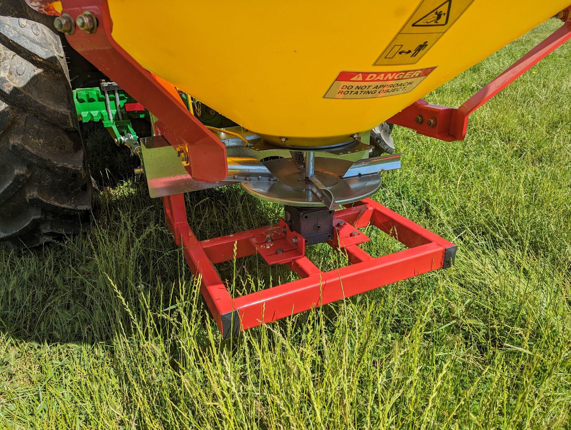A yellow and red tractor spreader is sitting in the grass