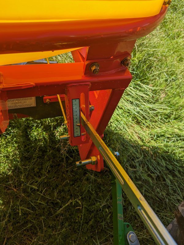 A red and yellow tractor is cutting grass in a field.