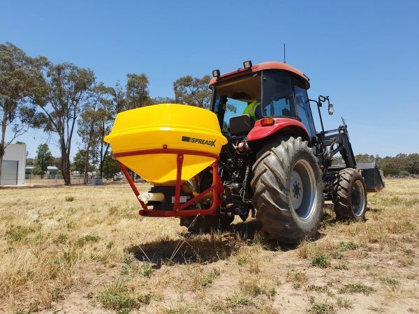 A red tractor with a yellow fertiliser attached to it
