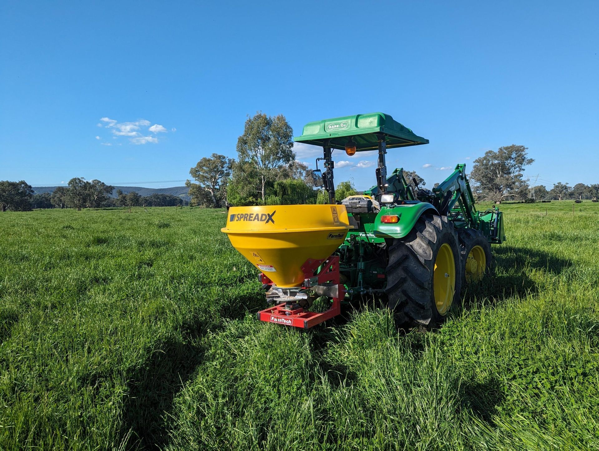 A green and yellow tractor is spreading fertiliser in a grassy field.