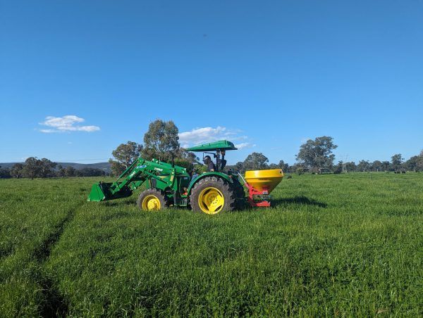 A green tractor is spreading fertiliser in a grassy field.