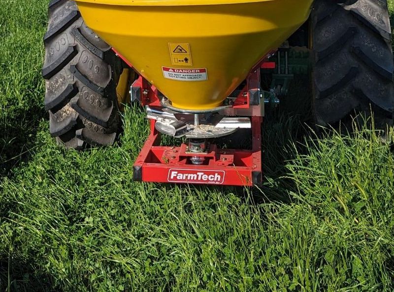 A tractor is spreading fertiliser on a lush green field.