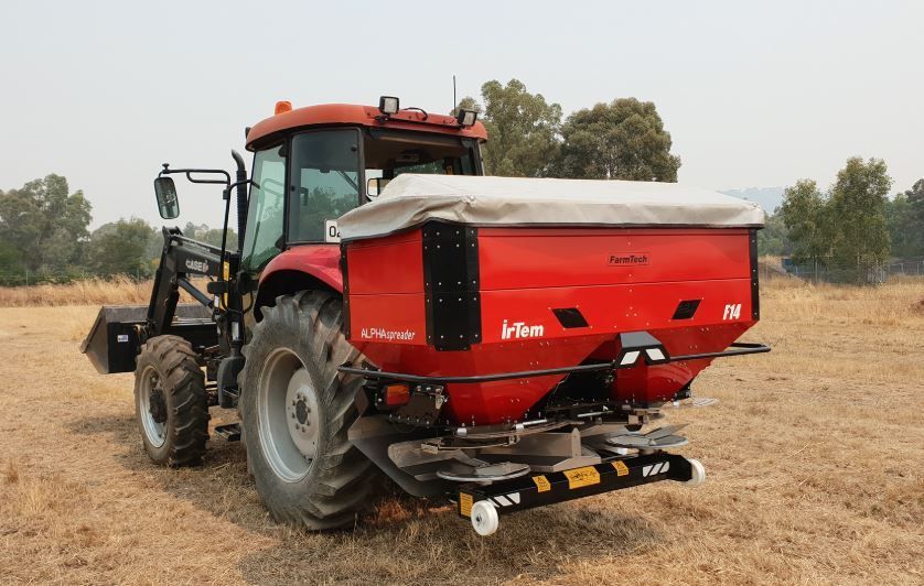 A red tractor is sitting in a field with a spreader attached to it.