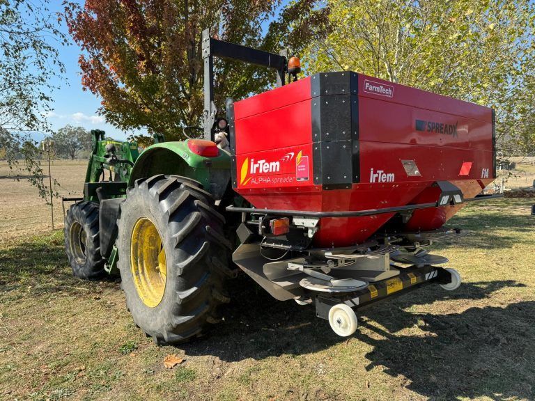 A john deere tractor with a red fertiliser spreader attached to it is parked in a field.