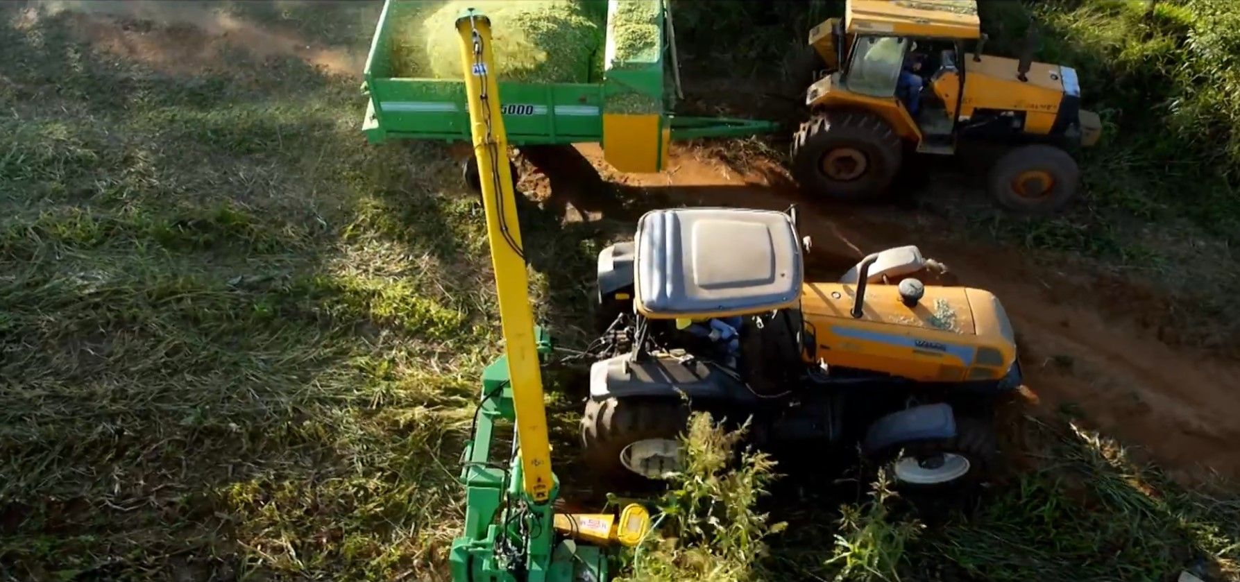 A tractor is cutting grass in a field with a machine attached to it.