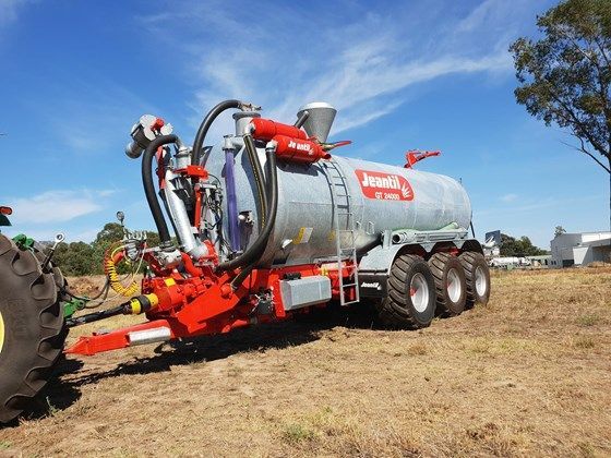 A john deere tractor is pulling a large tank in a field