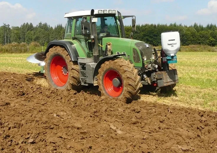 A green and red tractor is plowing a field