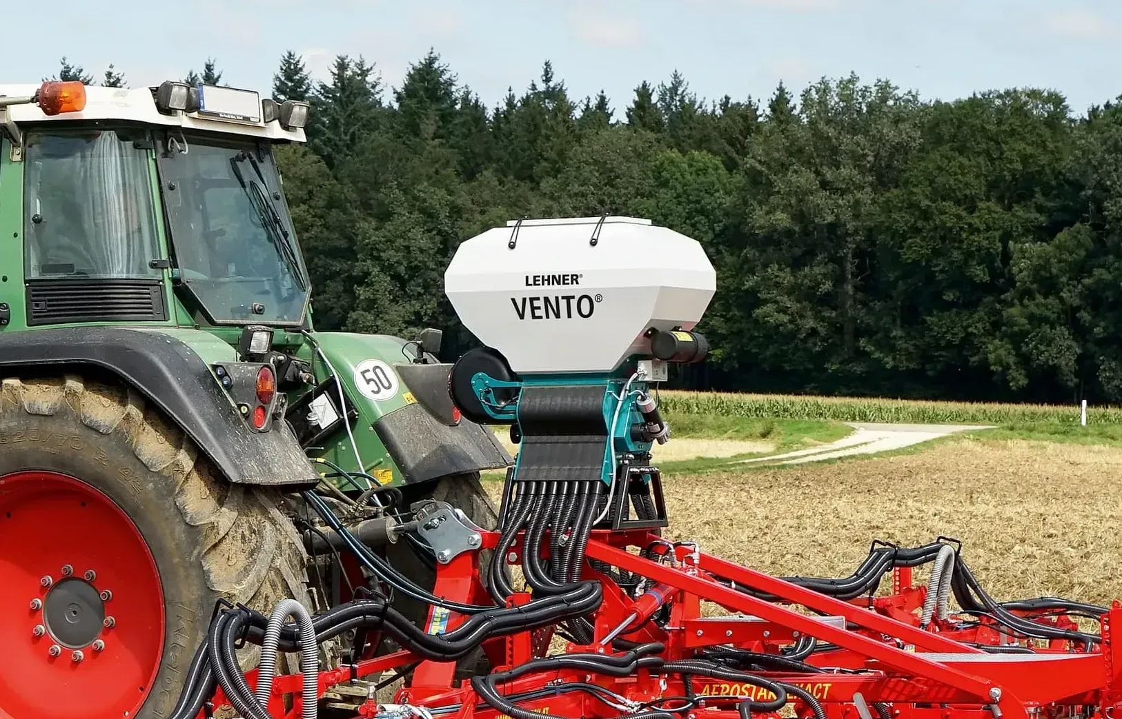 A green and red tractor is plowing a field.
