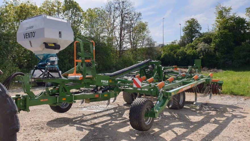 A green tractor with a trailer attached to it is parked in a dirt field.