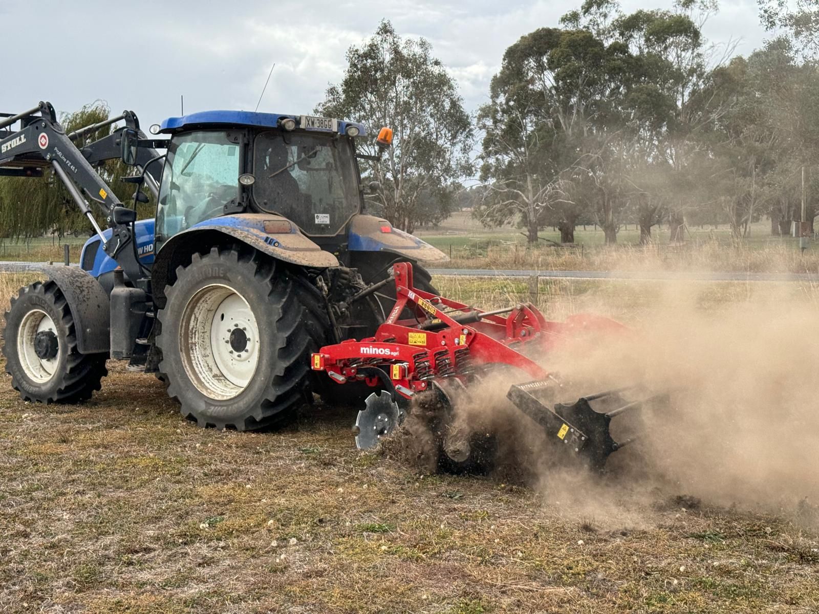 A blue and yellow tractor is towing a disc tiller in a field.