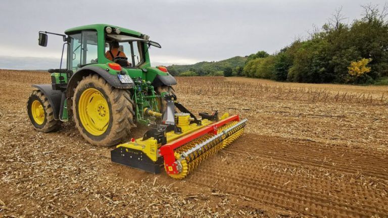 A green and yellow tractor is plowing a field.