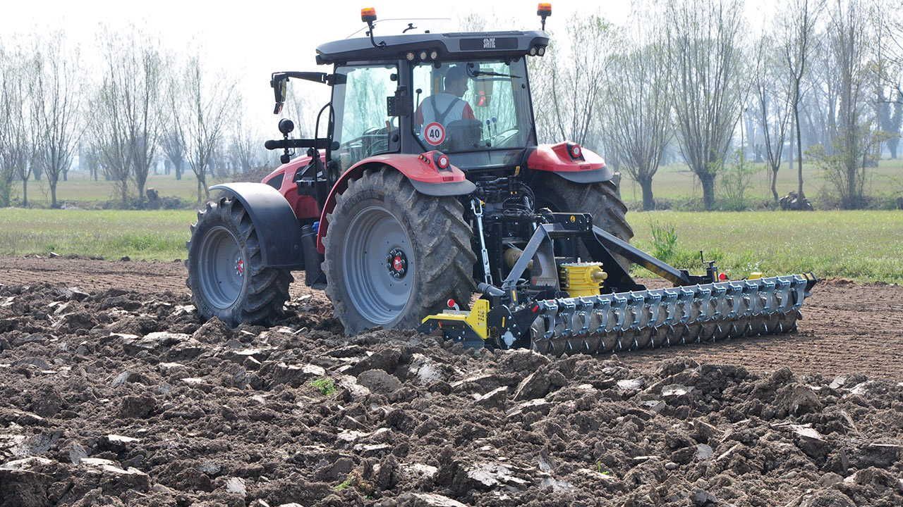 A red tractor is plowing a field with a plow attached to it.