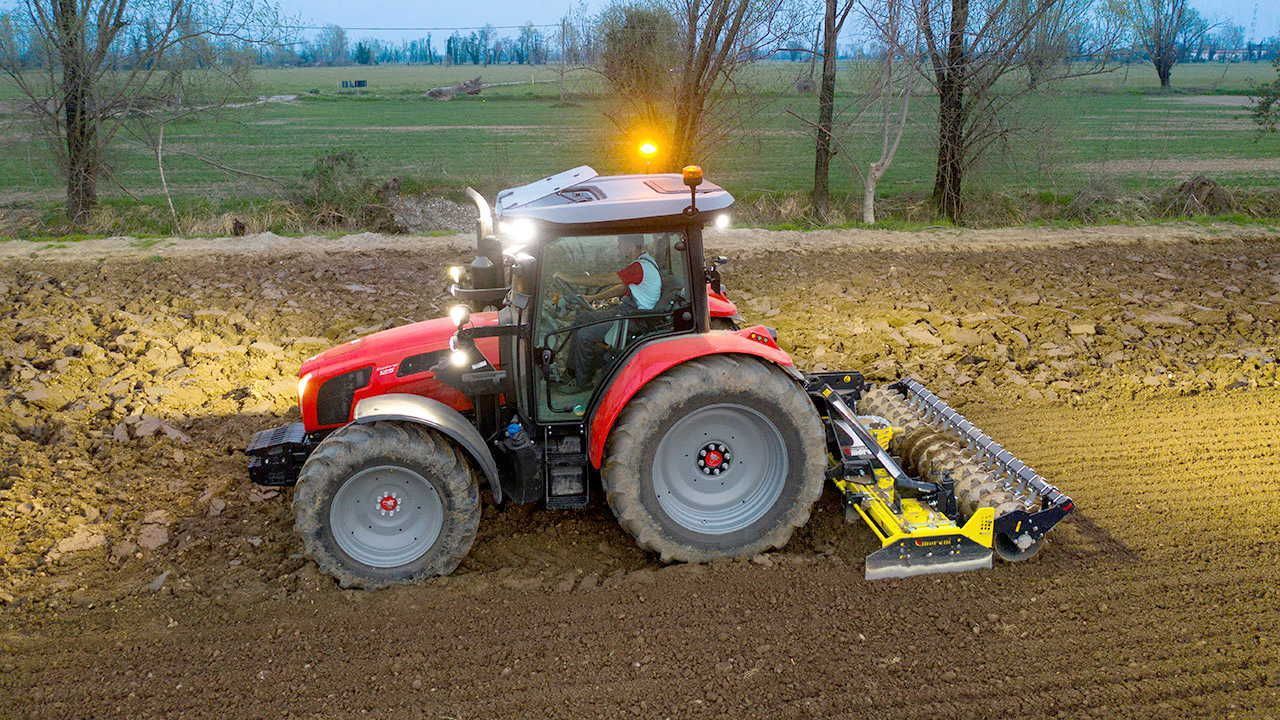 A red tractor is plowing a field at night.