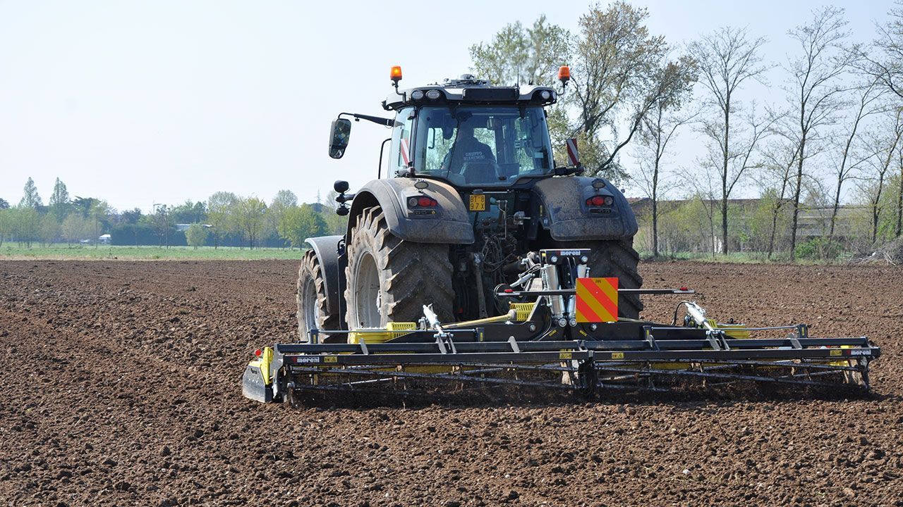 A tractor in a field with a power harrow attached to it.