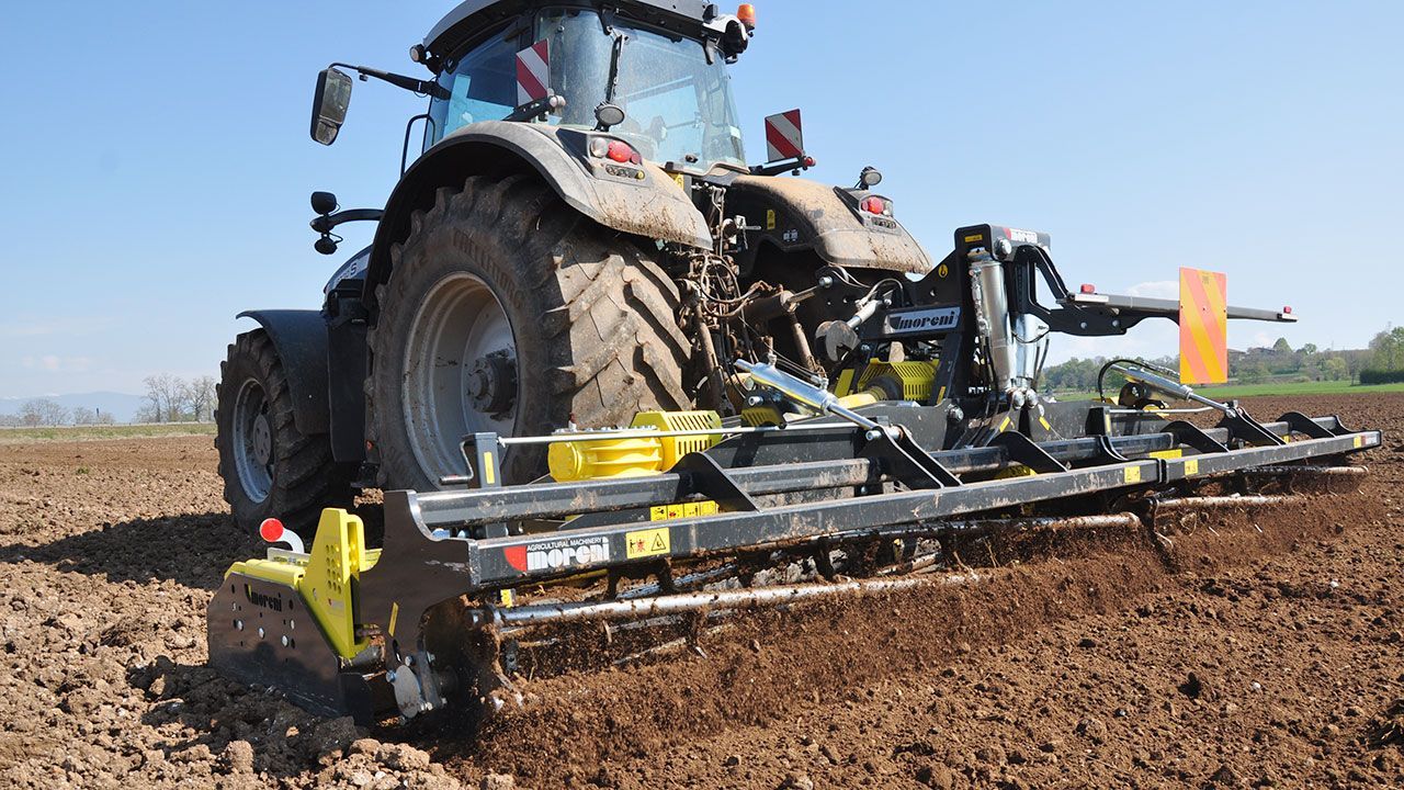 A tractor in a field with a power harrow attached to it.