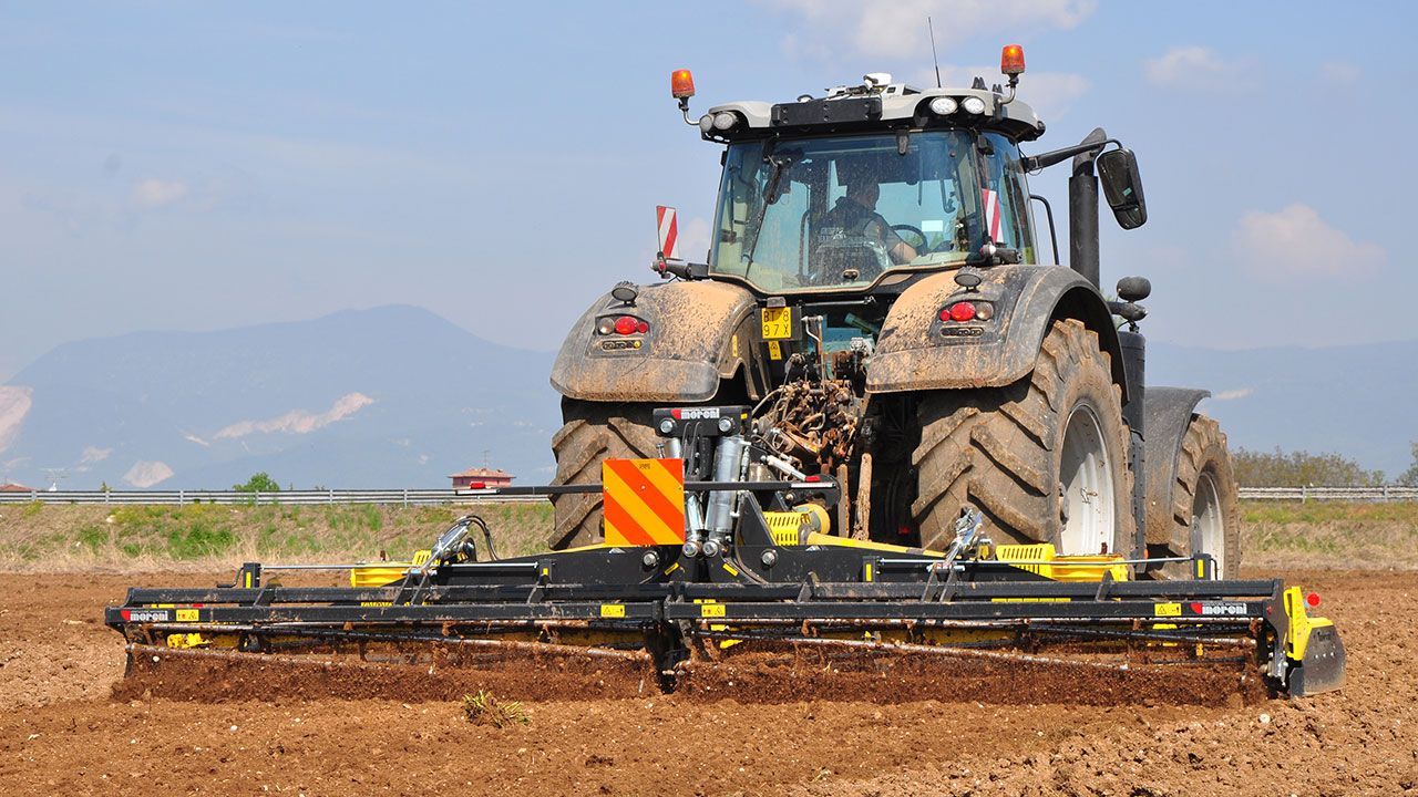 A tractor in a field with a power harrow attached to it.