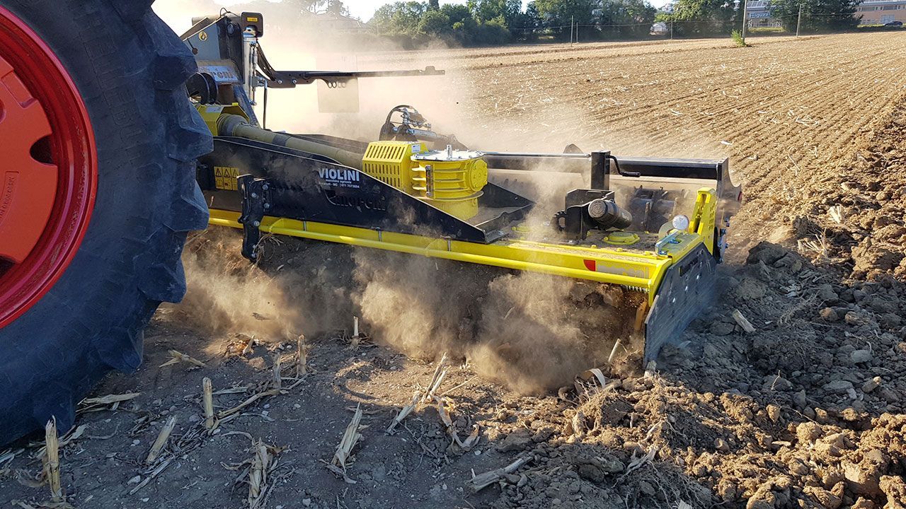 A tractor in a field with a power harrow attached to it.