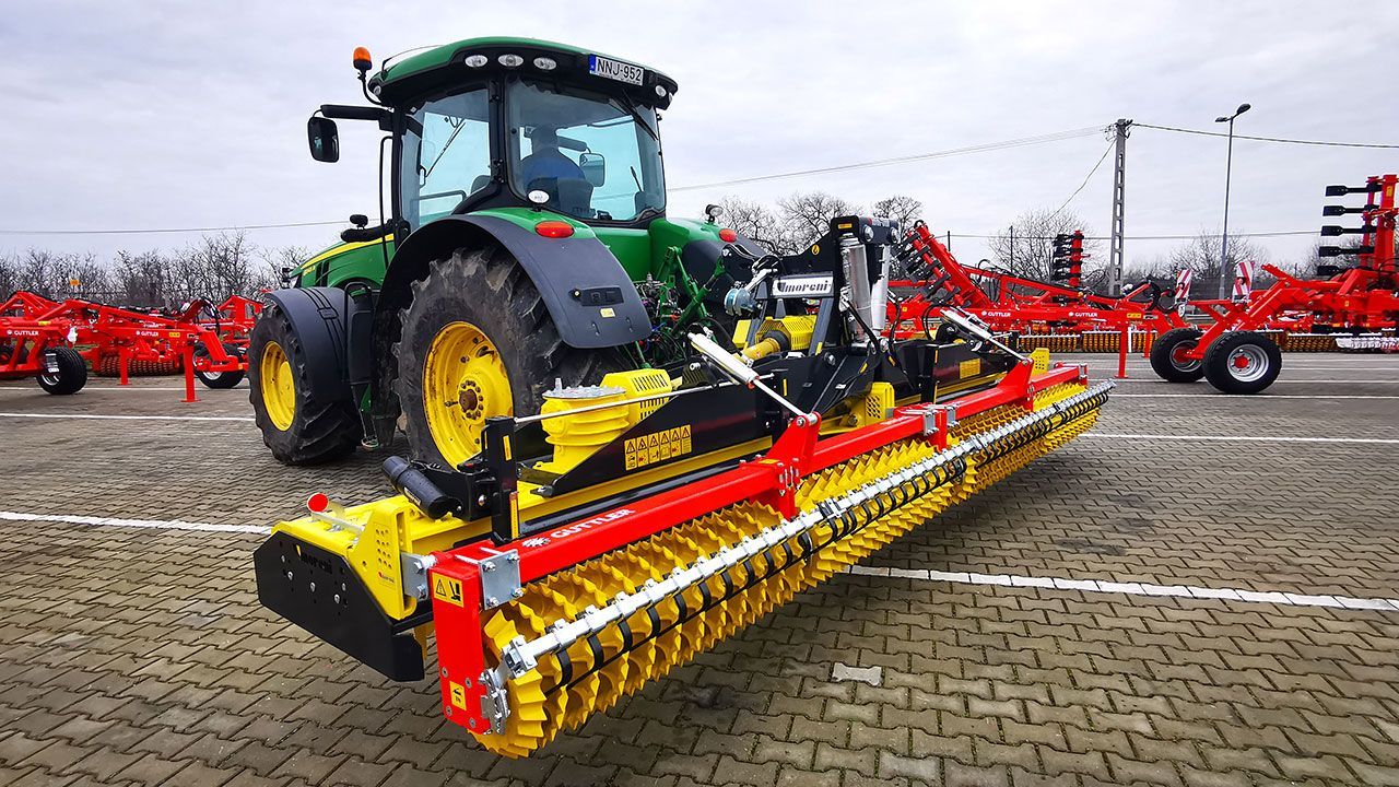 A tractor on a brick road with a power harrow attached to it.