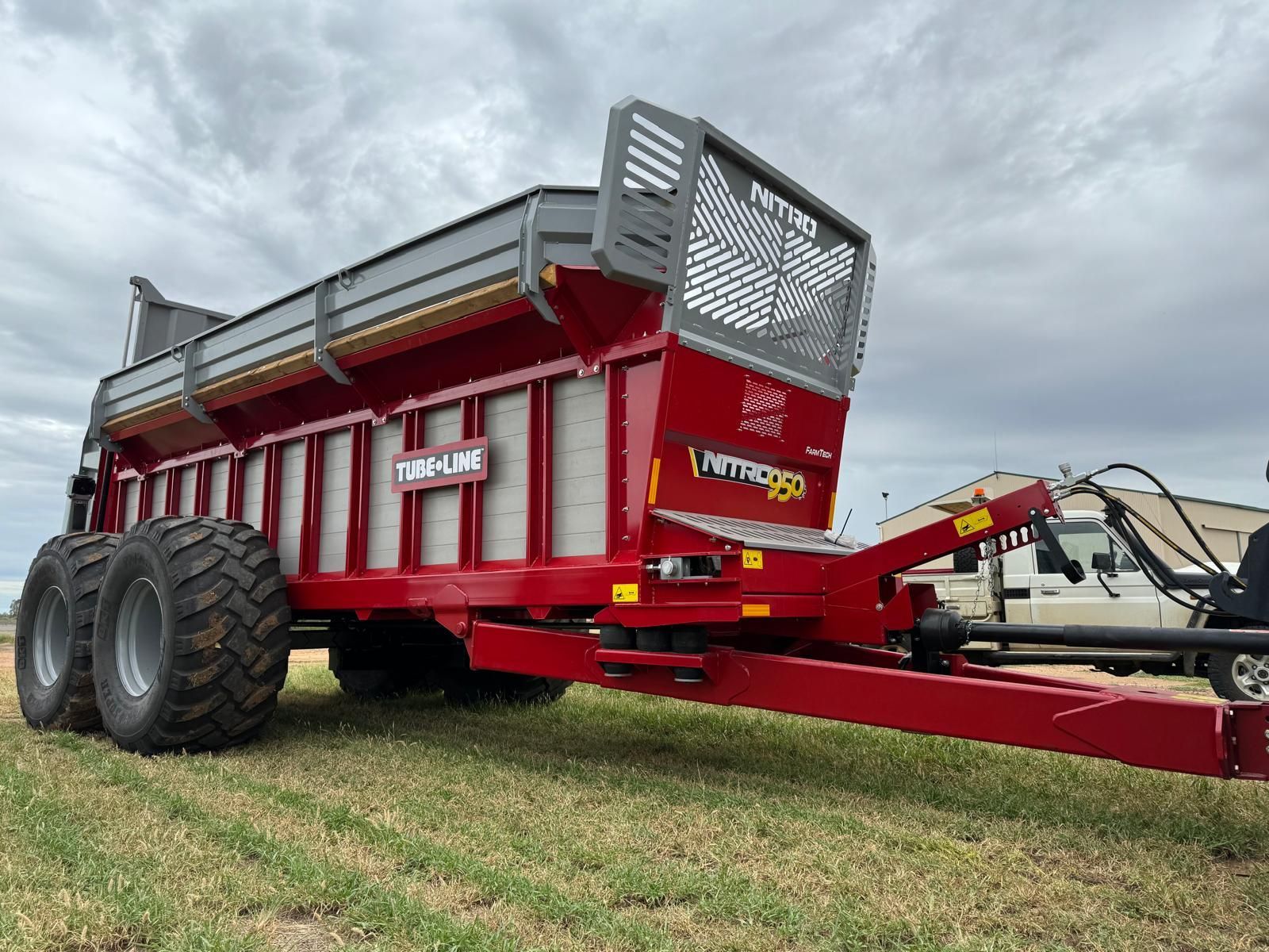 A red trailer is parked in a field next to a truck.
