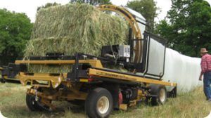 A man is standing next to a machine that is wrapping hay in plastic.