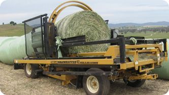A man is standing next to a machine that is wrapping hay in plastic.