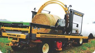 A man is standing next to a machine that is wrapping hay in plastic.
