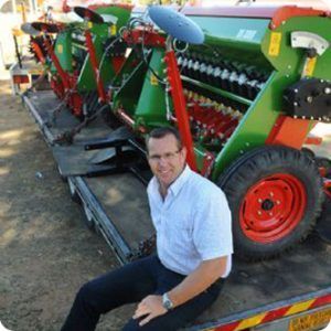 A man is sitting on the back of a truck next to a row of tractors