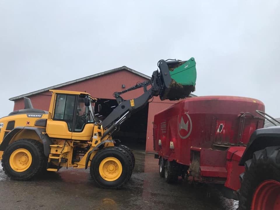 A yellow tractor is loading a red feed mixer with a green bucket.
