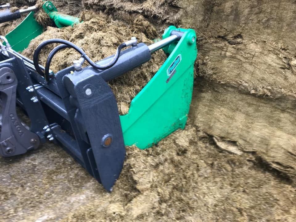 A green and black bucket is sitting on top of a pile of silage