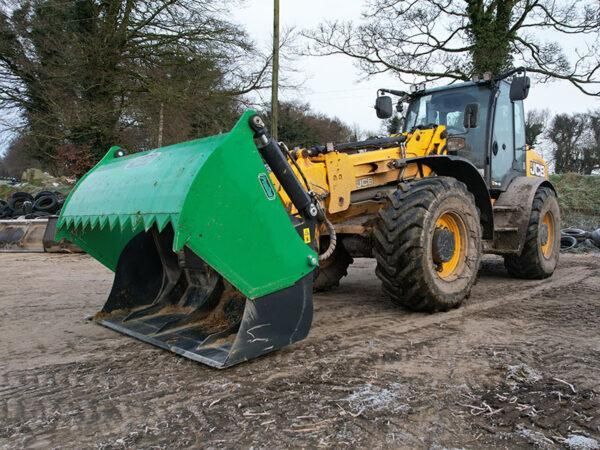 A yellow and black tractor with a green bucket is parked in a dirt field.