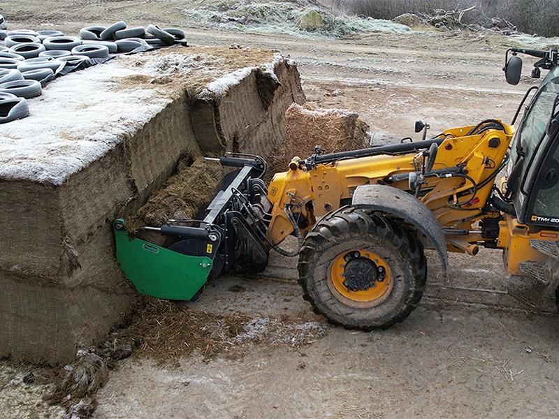 A yellow tractor is loading hay into a pile of tires.