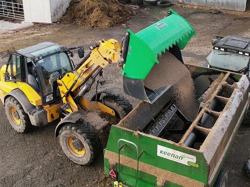 A yellow tractor is loading sand into a green trailer.