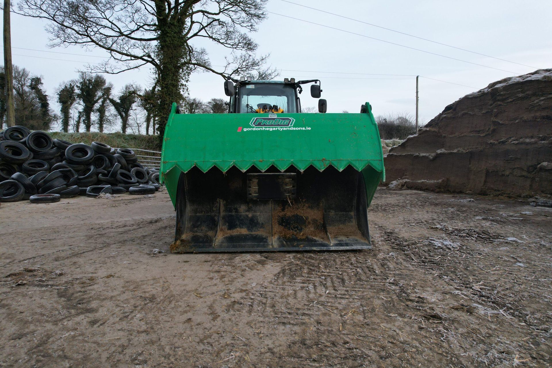 A green tractor is parked in a dirt field next to a pile of tires.