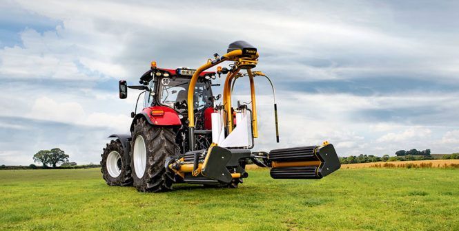 A red tractor is wrapping hay in a field.