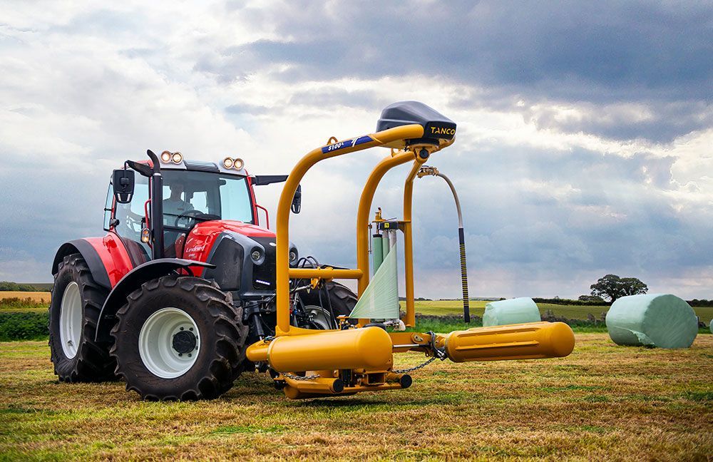 A red tractor is wrapping bales of hay in a field.