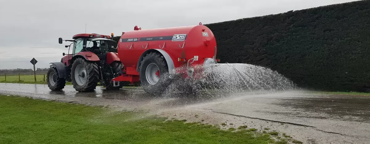 A red tractor is spraying water on a muddy road.