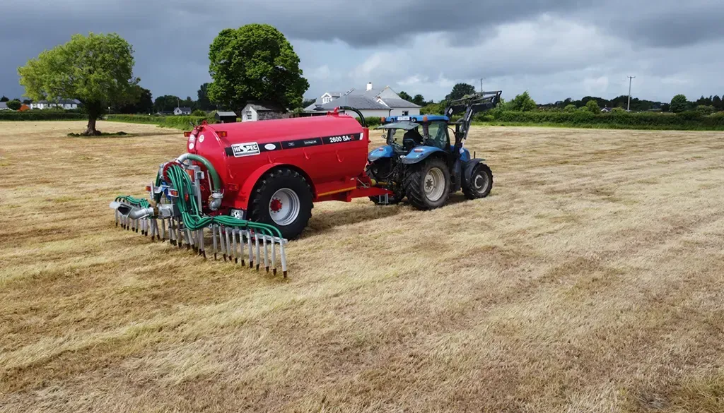 A tractor is plowing a field with a red tank attached to it.
