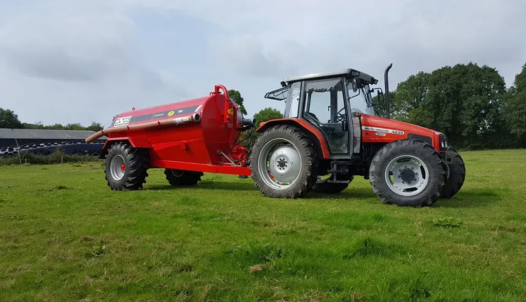 A red tractor is parked in a grassy field with a trailer attached to it.