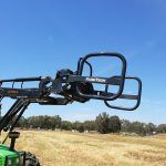 A green tractor is parked in a field with a forklift attached to it.