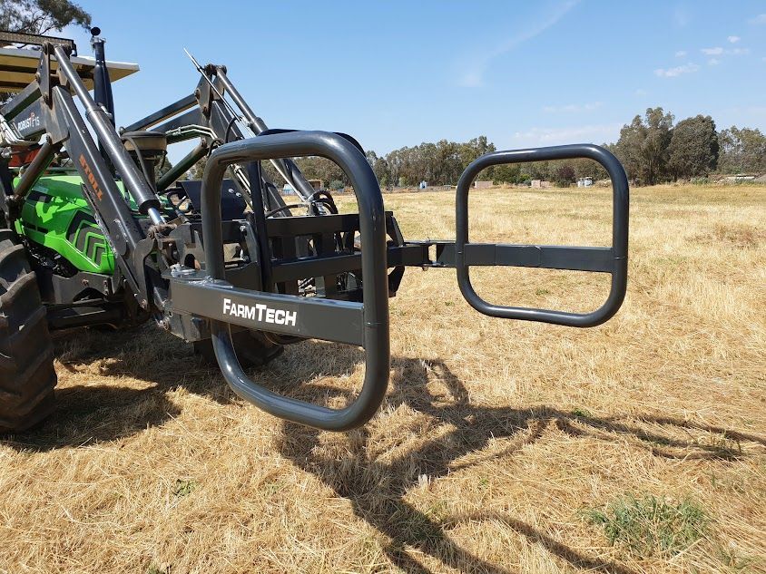 A tractor is sitting in a field with a hay bale clamp attached to it.