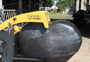 A yellow tractor is holding a bale of hay wrapped in plastic.