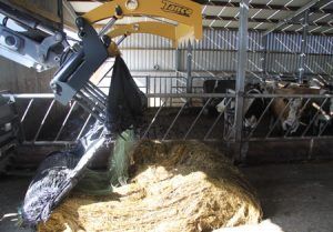 A large pile of hay is being scooped out of a machine in a barn.
