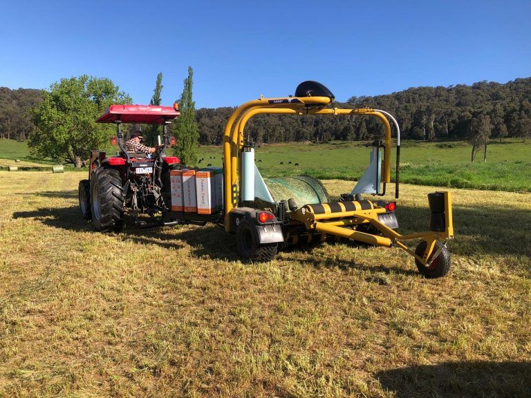 A tractor is wrapping hay on a trailer in a field.